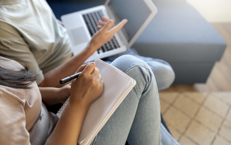 woman writing on notepad next to man on computer