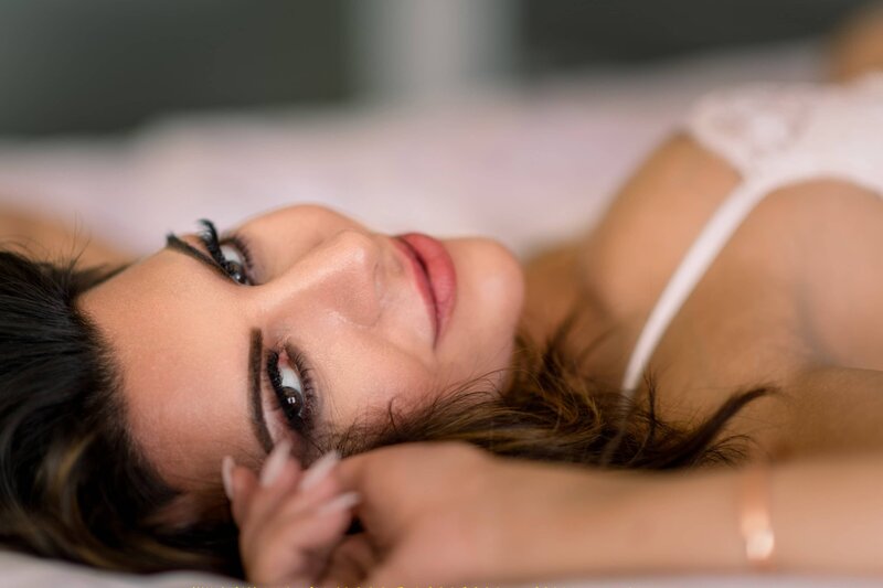 Close up of a womans face as she lays on a bed and looks at the camera