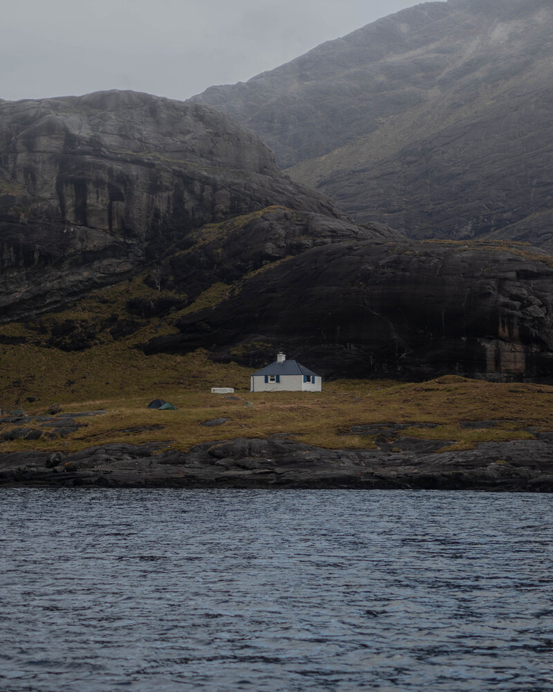 single small home on isolated harsh rocky island with deep blue water surrounding the island