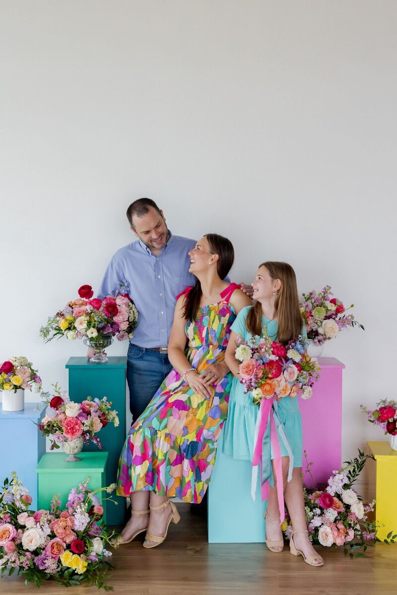 Tamara Menges with husband and daughter, sitting among colorful pastel blocks and joyful floral designs.