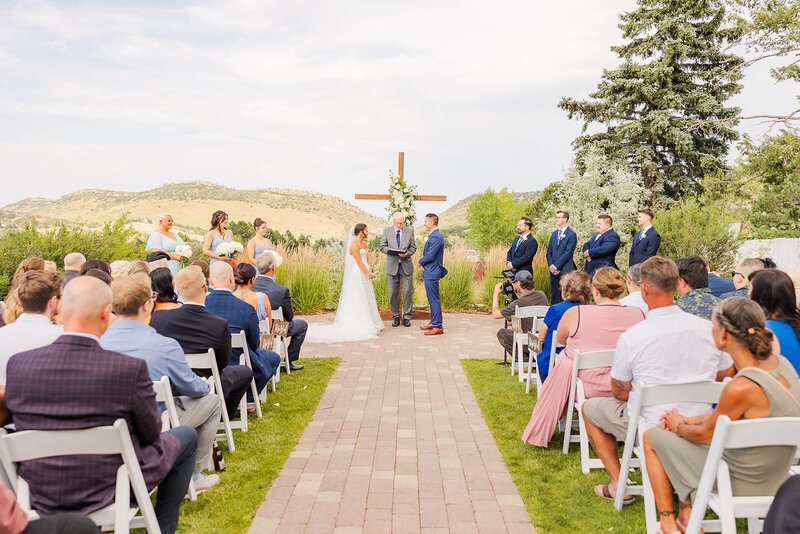 Emotional bride and groom exchanging vows during their wedding ceremony at The Manor House in Littleton, Colorado, surrounded by a stunning outdoor setting and cherished family and friends.