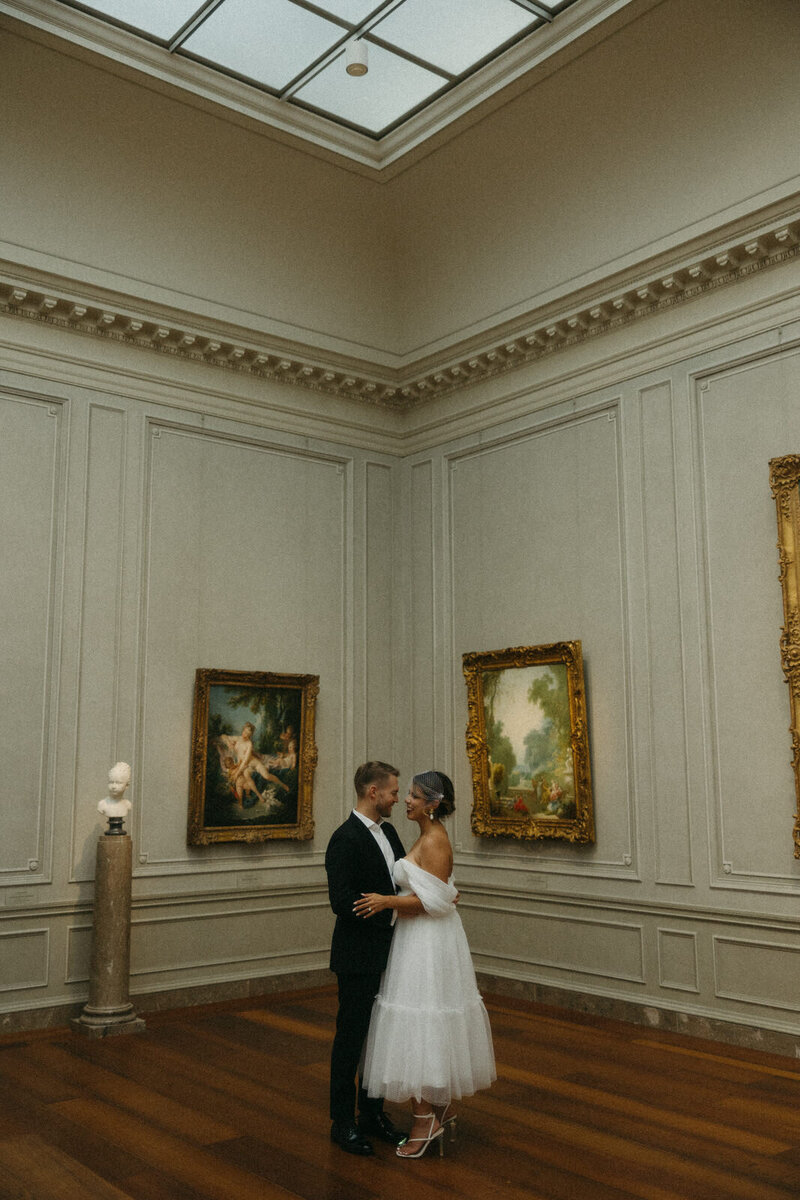 Bride and groom gholding each other on their wedding day while taking portraits in the National Gallery of Art in Washington DC, photographed by Andrea-Marie Photography