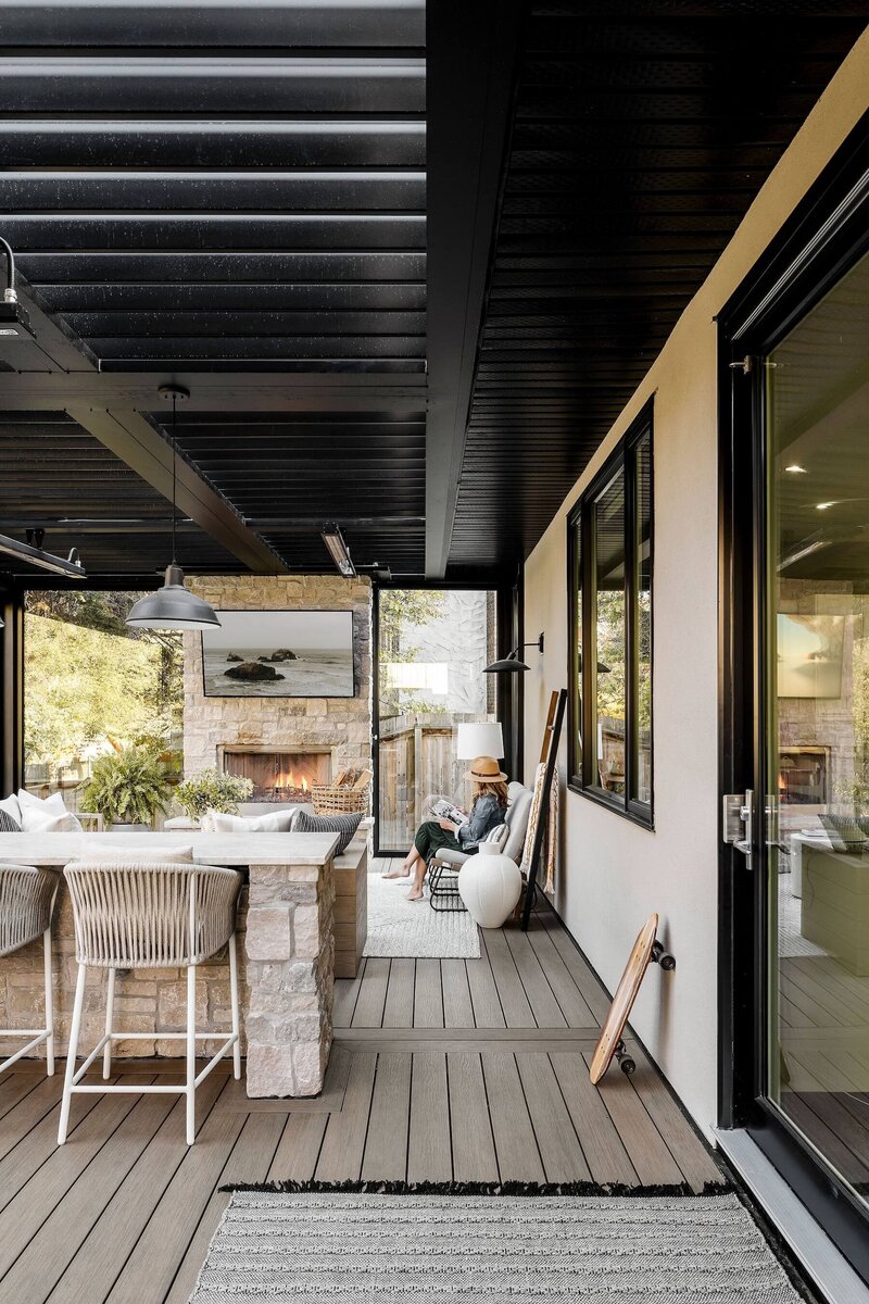 An outdoor bar with stone accents, rattan stools and black pendant lighting under a suncoast enclosure.