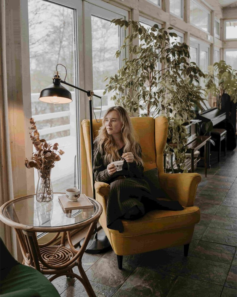 Femme assise dans un fauteuil jaune avec une tasse de thé, en pleine réflexion intérieure, illustrant l’invitation à laisser son âme devenir sa boussole et à avancer avec plus de clarté et de connexion intérieure.
