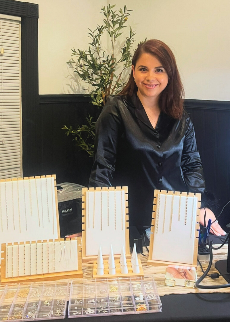 Permanent jewelry artist Denisa at her pop-up booth with chain display boards and charm organization.