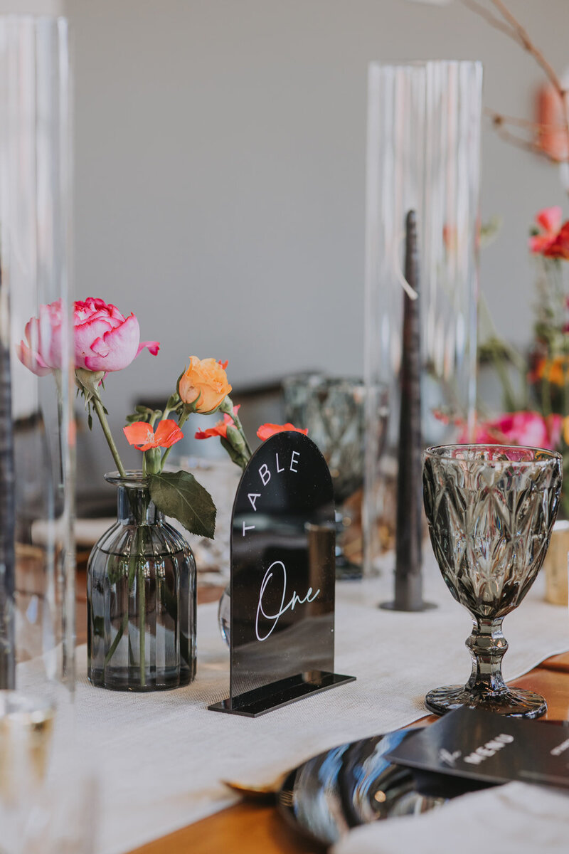 Close-up of luxury wedding table decor with black plates, gold cutlery, crystal glasses, and vibrant florals at a Canmore venue.