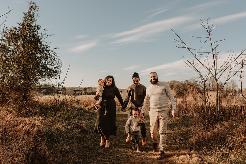 A family of five holding hands and smiling as they walk along a trail 