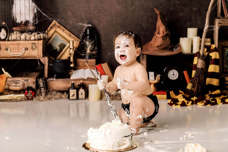 Portrait Photographers CT capture playful Harry Potter themed first birthday cake smash with baby wielding wand among vintage magical props