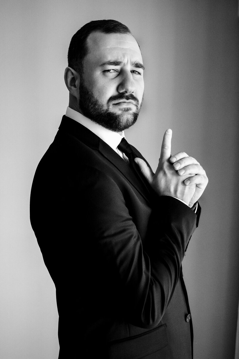 Black and white portrait of a groom posing like 007 with a finger gun  in Atlanta, GA tby Charlotte wedding photographers DeLong Photography