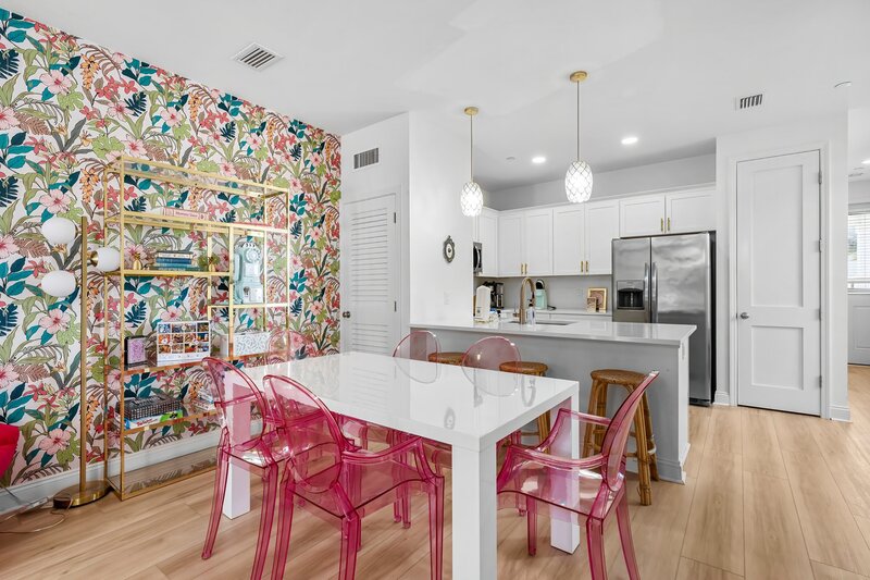 Modern kitchen with stainless steel appliances and white countertops opens into a playful dining space with pink chairs—great for group meals near Alys Beach and 30A.