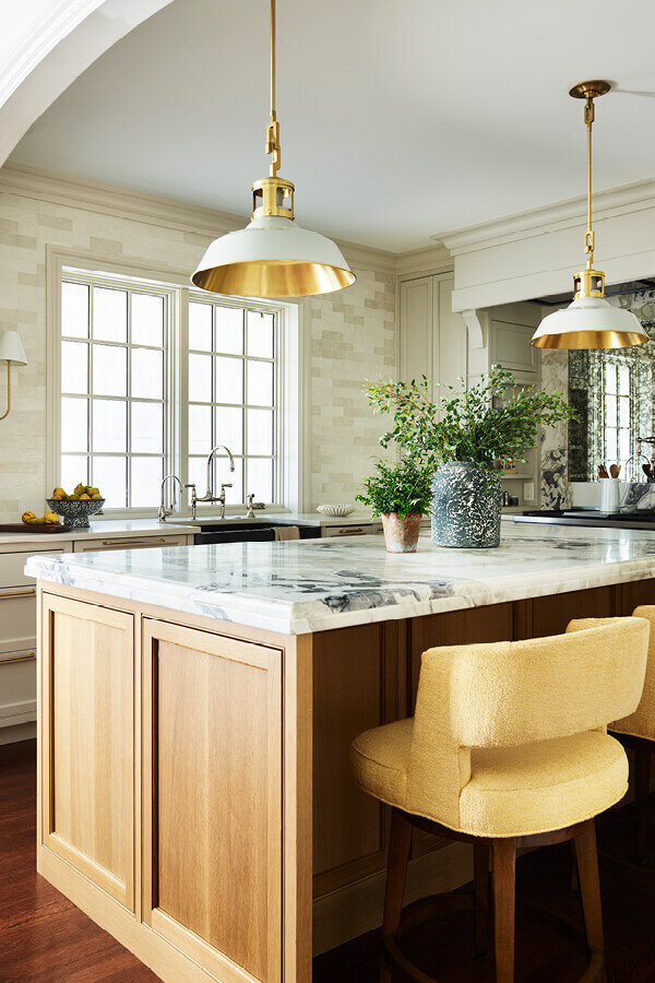 A traditional kitchen design in Milton featuring white kitchen cabinets, a natural oak island, custom yellow stools, and a brass light fixture for warmth and charm.