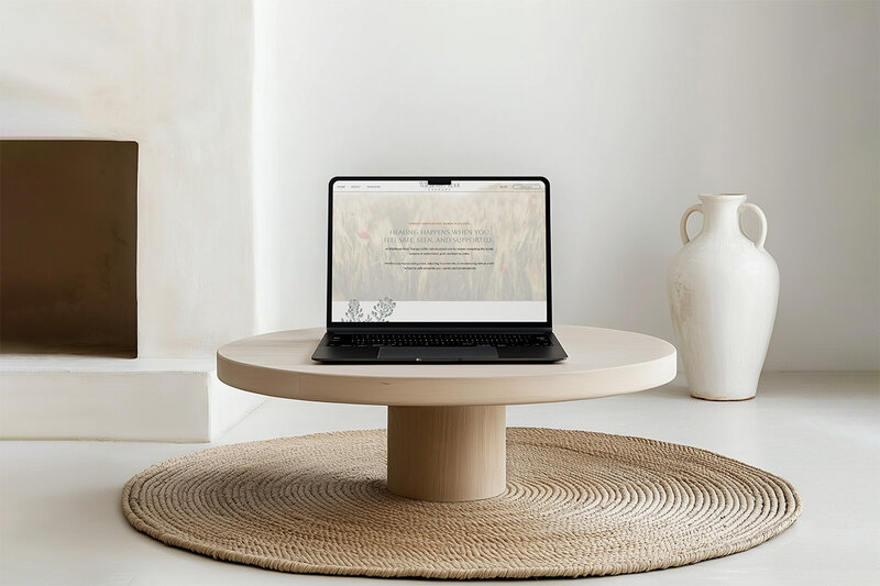 Laptop on a round table in a bright white room, designed for a mental health website.