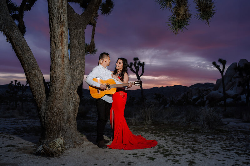 Joshua Tree Elopement with Asian couple during sunset blue hour at Hidden Valley holding playing guitar.