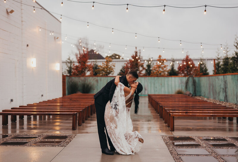 Wedding photo of couple kissing in front of rows of empty benches