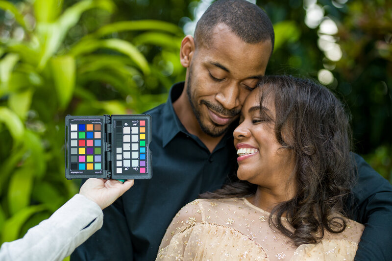 A photographer holding up a gray card to balance white balance during an engagement session, ensuring accurate and vibrant colors for stunning and professional engagement photos.