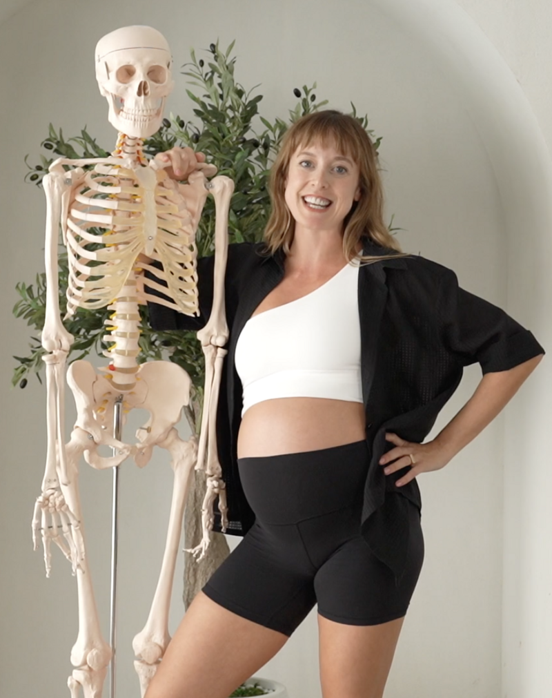 Alice stands confidently next to a skeleton model, embodying the knowledgeable yet accessible spirit of the anatomy-informed yoga practices she teaches.