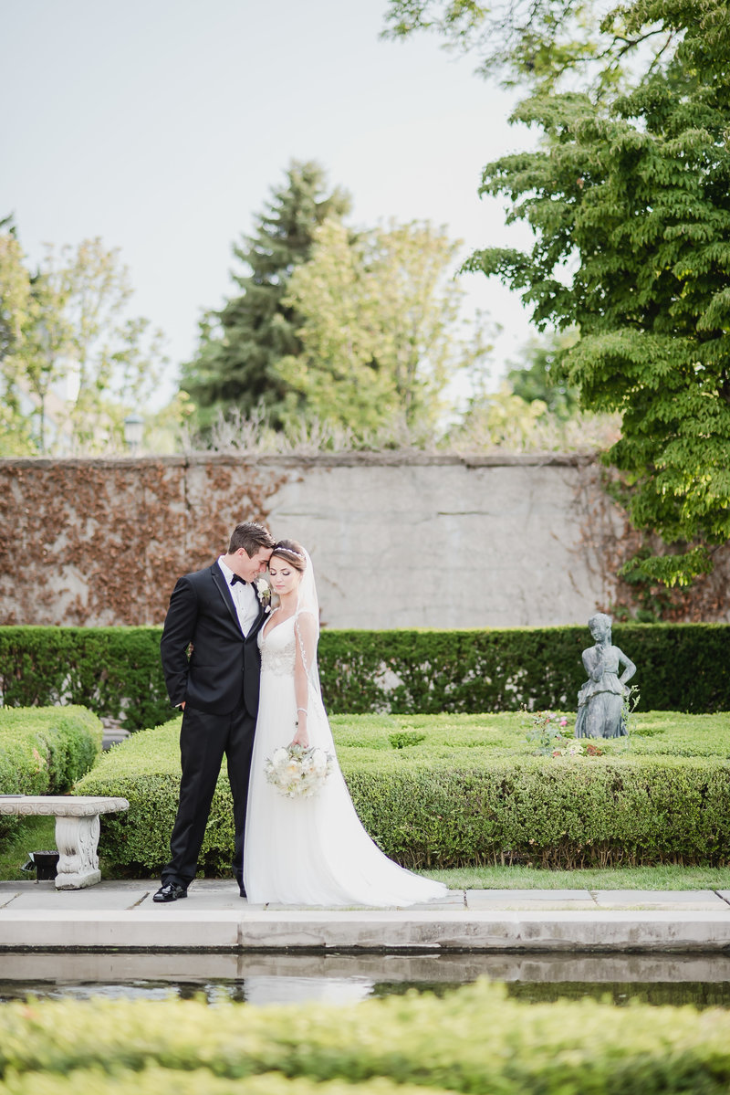 Bride and groom share a quiet moment in the formal gardens at The War Memorial in Grosse Pointe, Michigan, surrounded by sculpted hedges and reflecting water