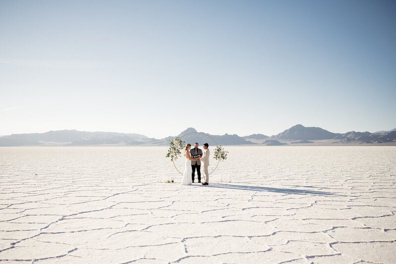 A salt flats elopement with a couple in the center of the photo with a circular arch and an officiant reading.