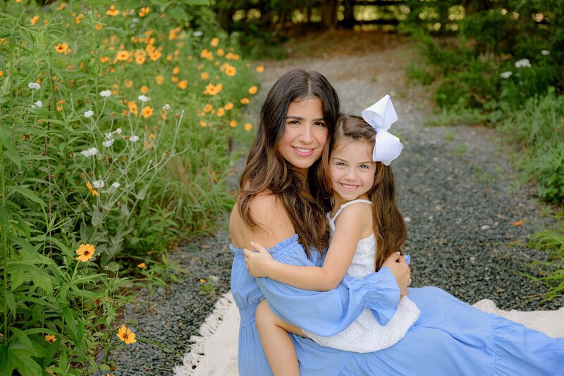 mother and daughter hug while sitting in a flower garden