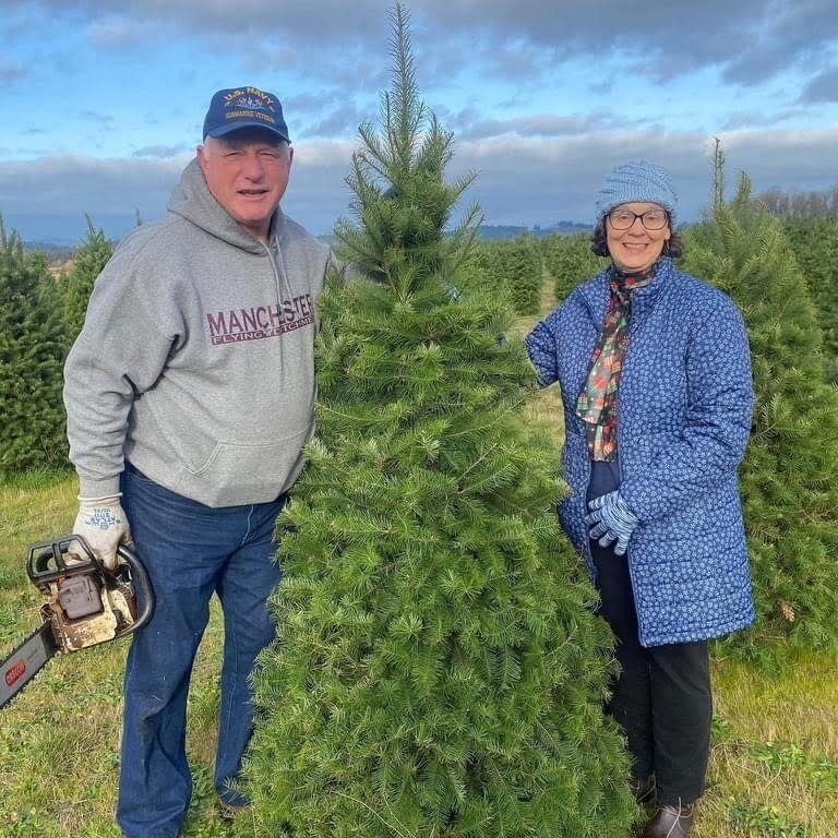 Local owners of Ecosystems, Janet and Buck Pelroy, smile whil standing by an evergreen tree.