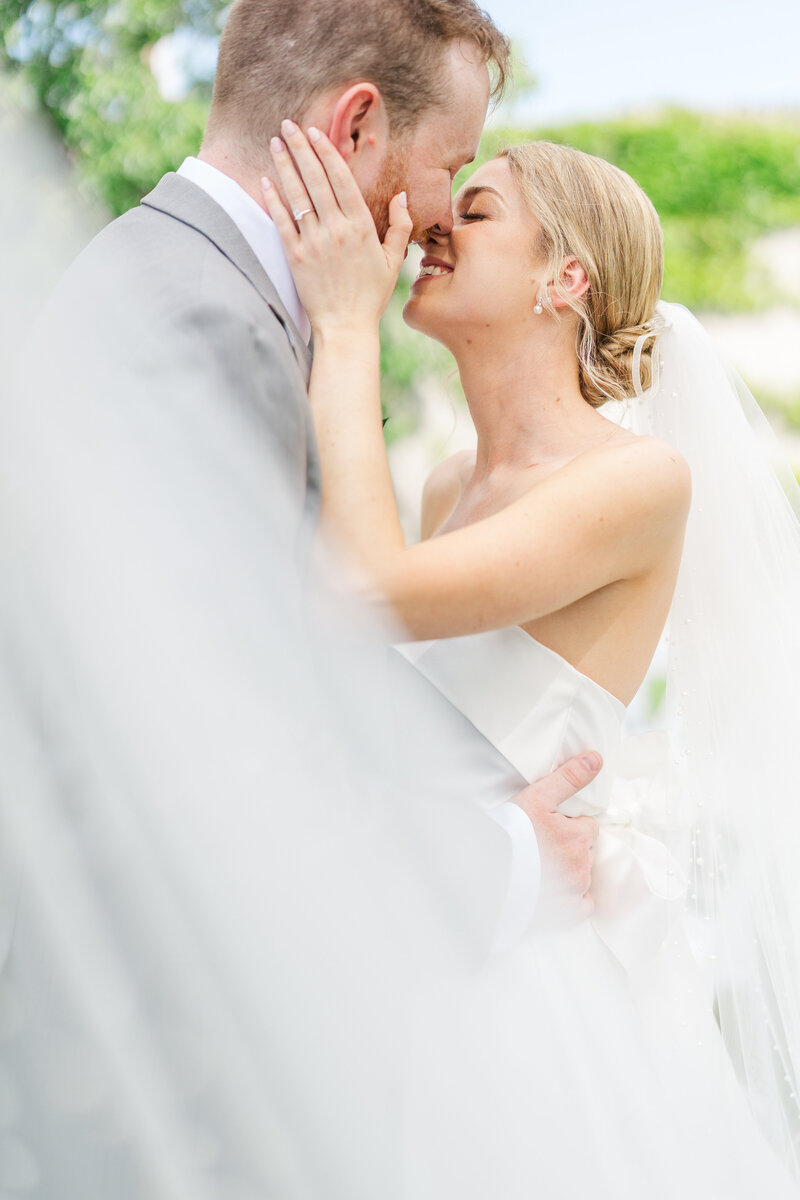 A man holds his fiancee as she smiles at the camera and he presses his forehead up against hers.