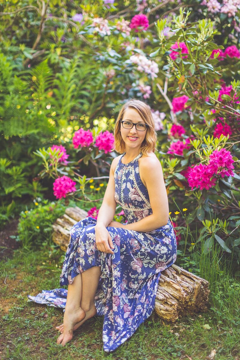 Chelsea Dawn sitting on a log in her garden with pink flowers.