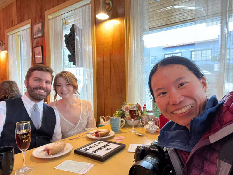 An eloping couple is sitting down with pie at a cafe and across from their photographer