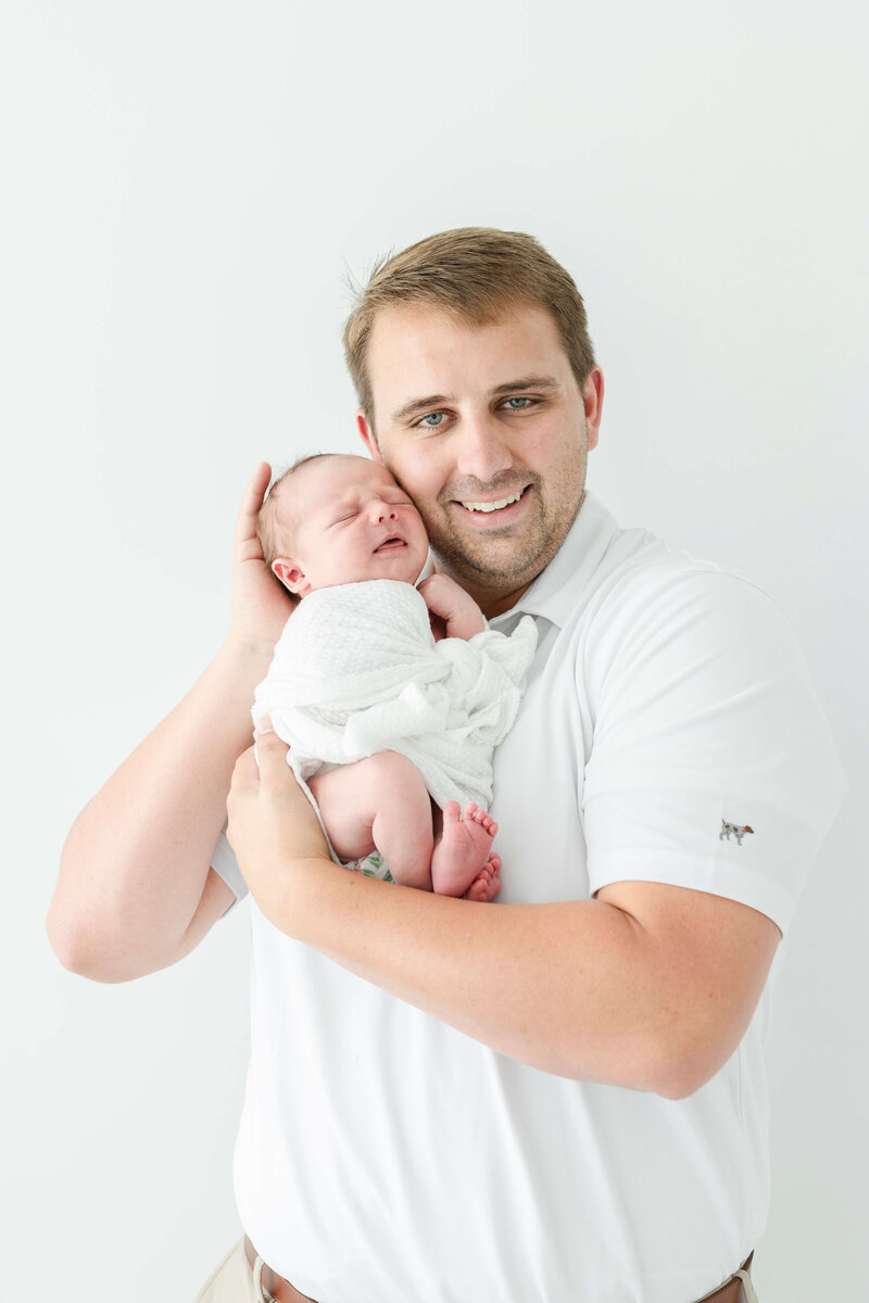 Dad holding newborn baby smiling at the camera during newborn photography session in Dothan Alabama