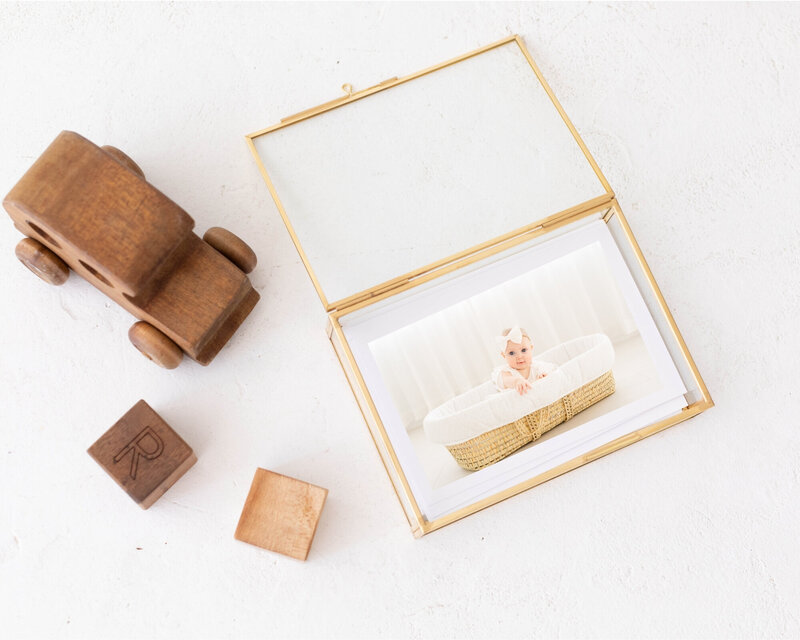 detail shot of gold glass photo box with a photo of a baby sitting in a moses basket.