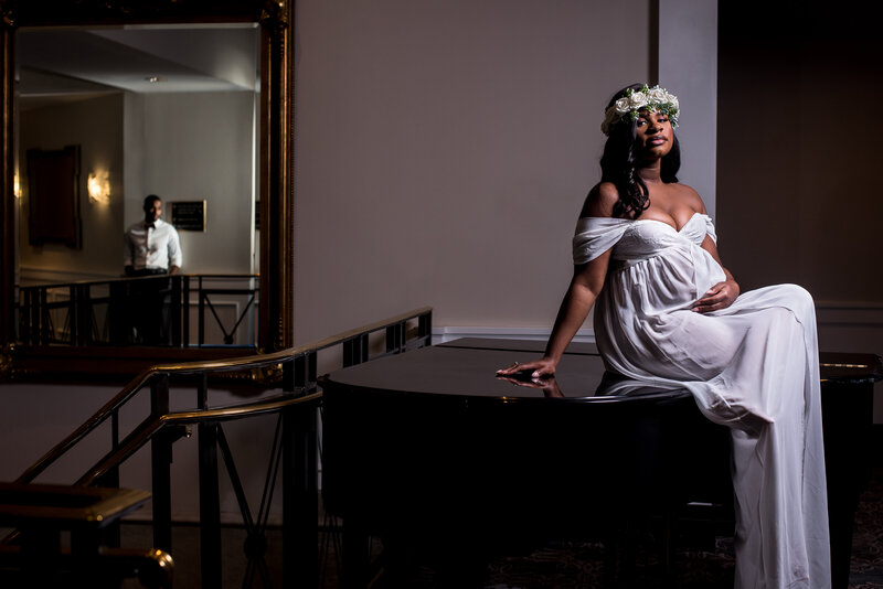 A woman poses on a piano wearing a white dress for her maternity photos