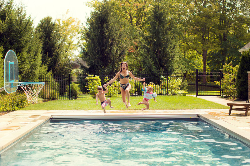 Mom and her two toddlers are jumping into the swimming pool at their backyard photo shoot.
