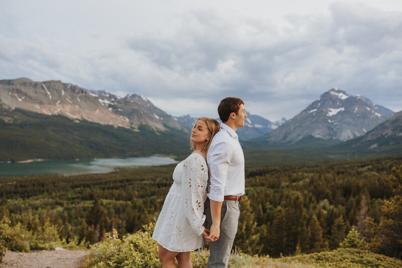 A couple posing back to back with Montana mountains in the background.