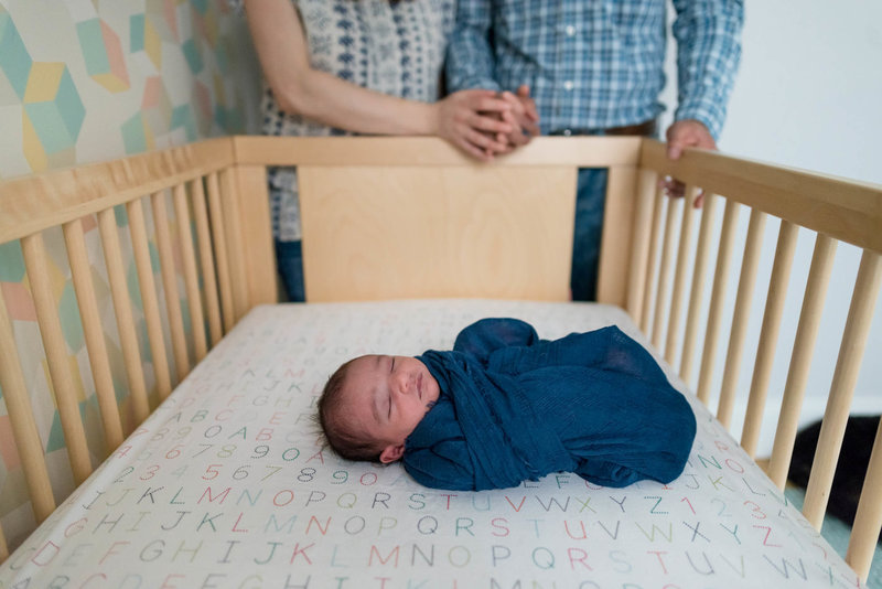 newborn in crib with parents hands