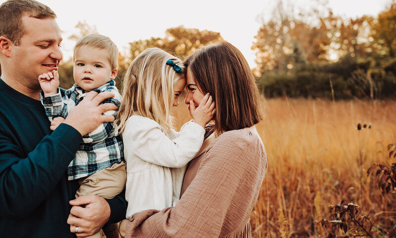 mom and daughter looking at each other, dad is holding baby, family session in Perrysburg metro park