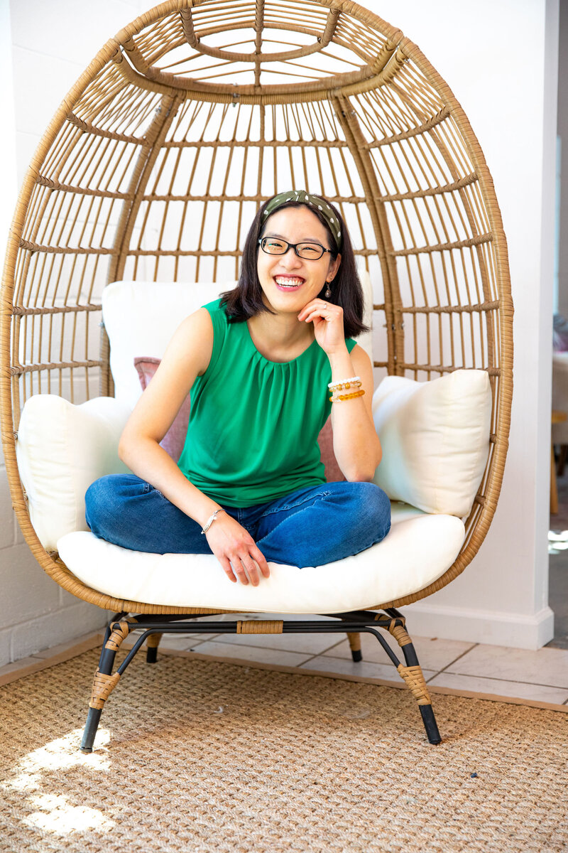 An Asian woman sitting and smiling in an egg chair.
