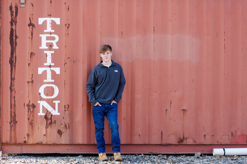 senior guy standing against an old train car, not on railroad tracks, photographed by Jamie lynette photography canton ohio senior photographer