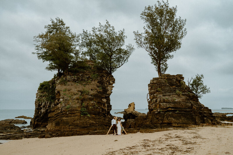 A & K standing side by side in front of alter on the beach in front of two large rock formations