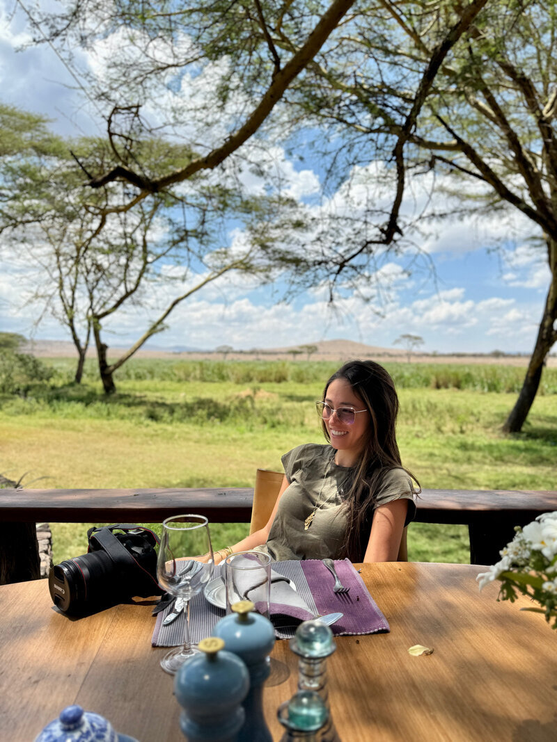 Chaya seated at a safari lodge with camera equipment, planning seamless bespoke journeys.