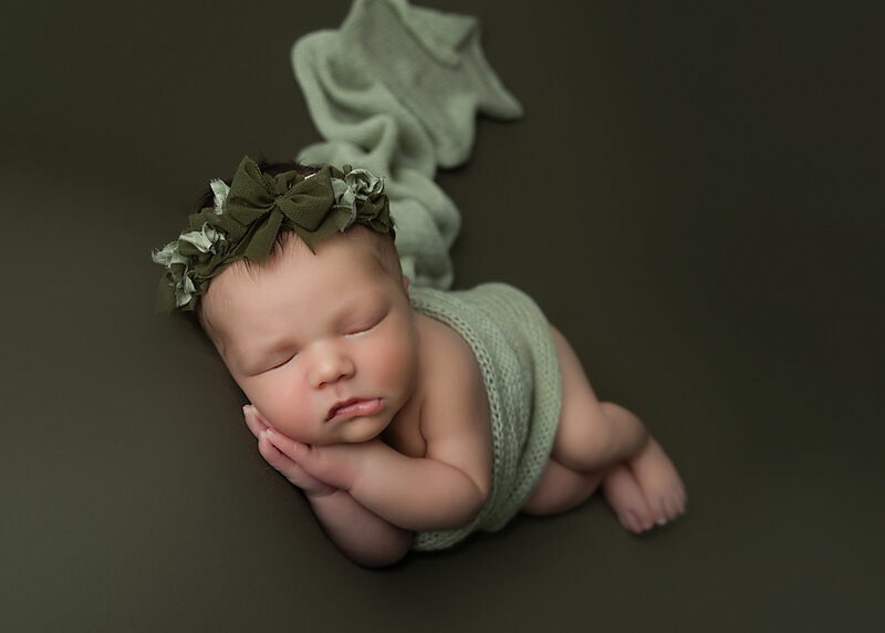 newborn baby girl in green wrap laying on side