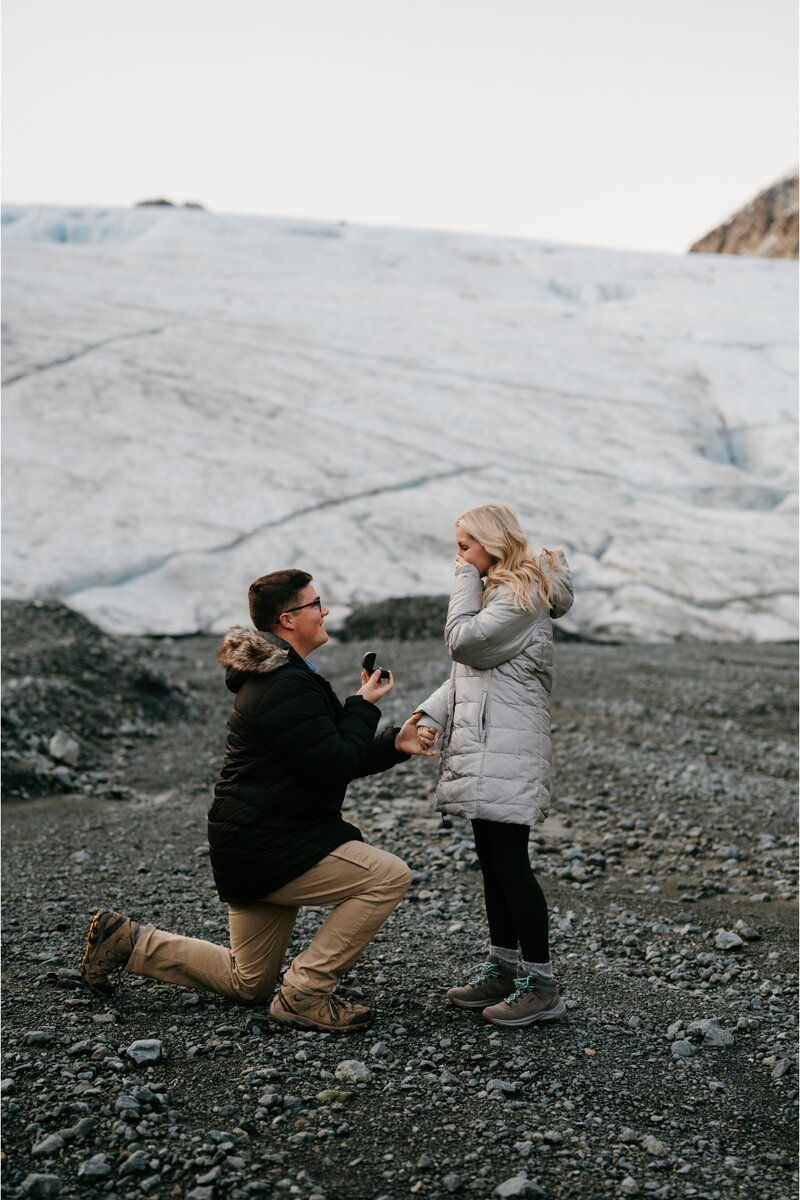Groom-to-be proposing on a glacier near Seward, Alaska, with champagne to celebrate the engagement.