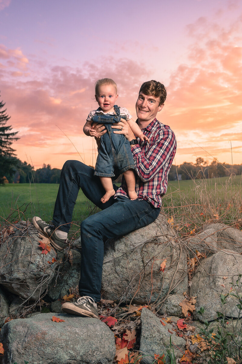 boston family photographer corey flint holding baby on stone wall at sunset