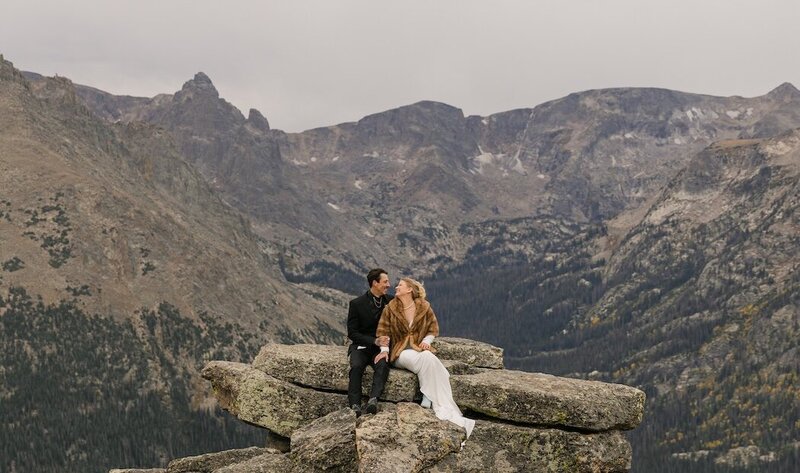 Elopement couple sitting on a rock ledge overlooking the mountains in Rocky Mountain National Park, photographed by a Colorado elopement photographer.
