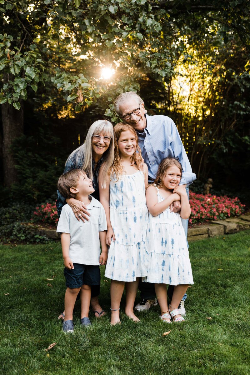Family of five with smiling grandparents and playful grandchildren enjoying a sunny day outdoors, captured by a talented family photographer in Pittsburgh, PA.