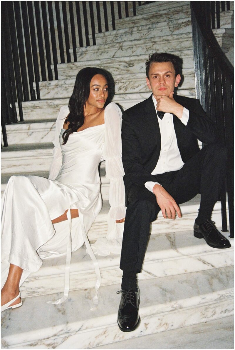 A bride and groom sit on a marble staircase leaning on each other captured by a Wilmington wedding photographer