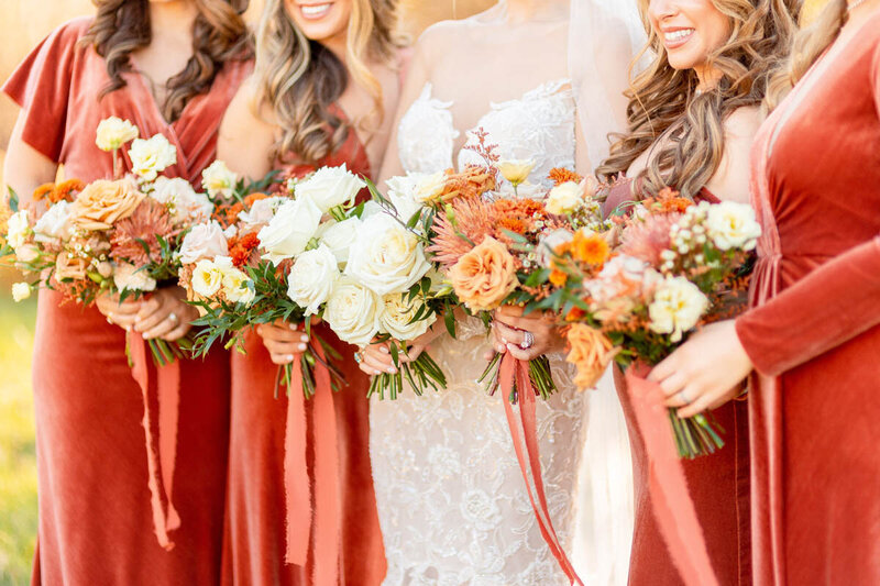 Bride and her bridesmaids laugh as they hold their bouquets.