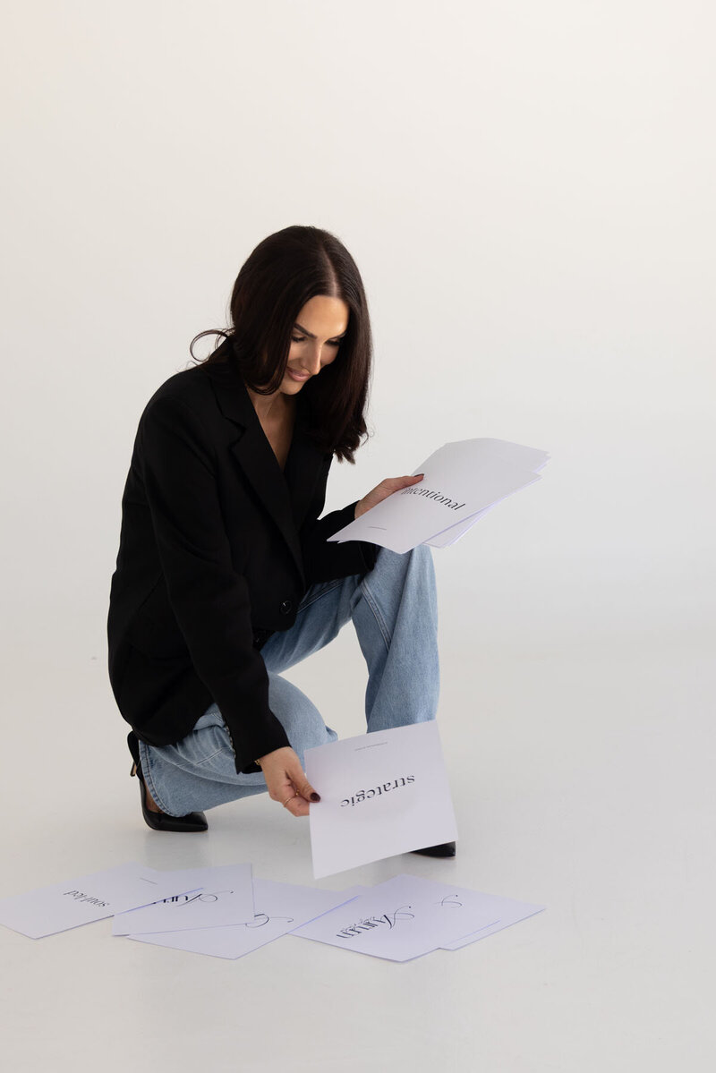 Tayla from Aurum Design Studio kneeling beside brand values and tone of voice printouts