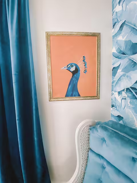 Striking framed peacock artwork with blue velvet headboard and curtains in a uniquely styled bedroom at Welcome to Paradise.