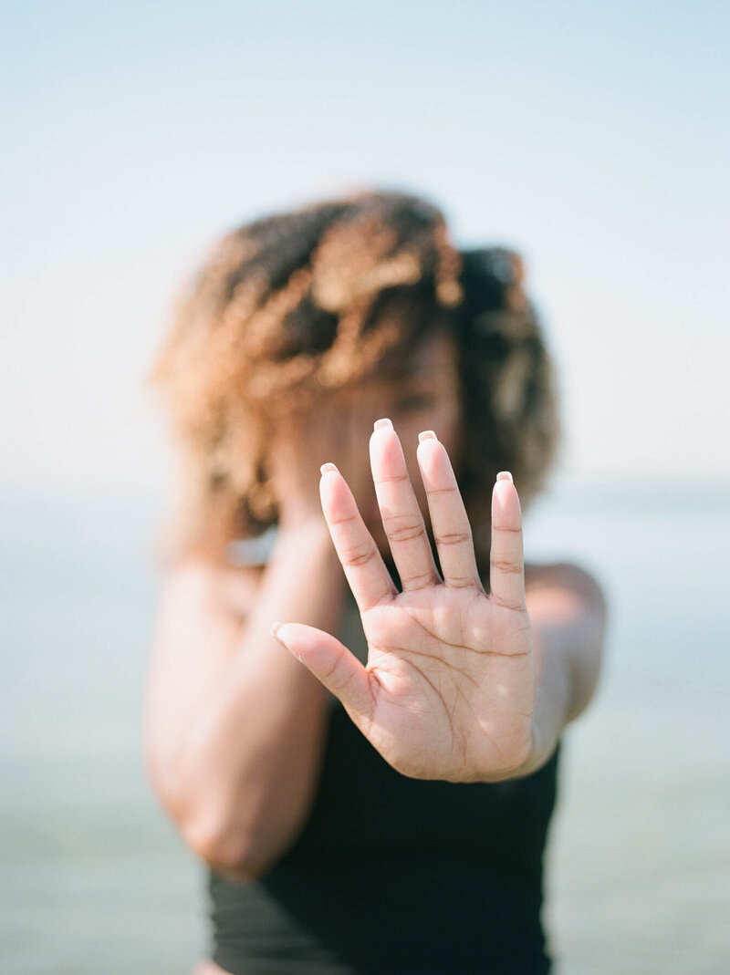 woman hiding her face with one hand and holding the other hand out as if to say "stop"