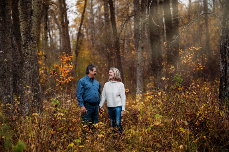 couple  holds hands standing in forest with sun streaming through trees