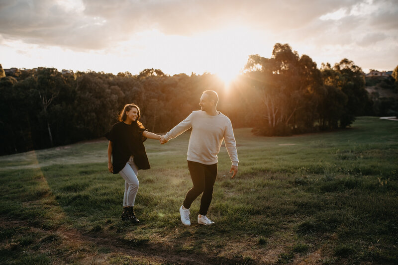 man leading woman through the park as the sun sets for their engagement shoot